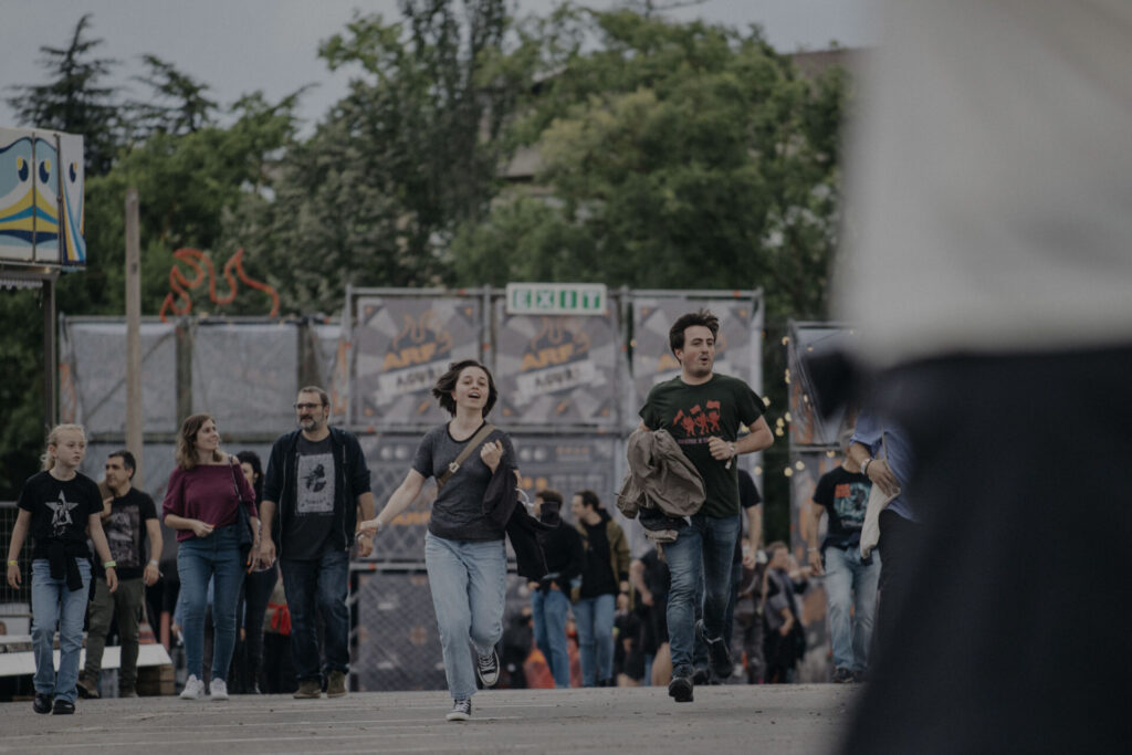 Grupo de asistentes entrando al Azkena Rock Festival, algunos caminando y otros corriendo, con el acceso principal y carteles del festival de fondo.